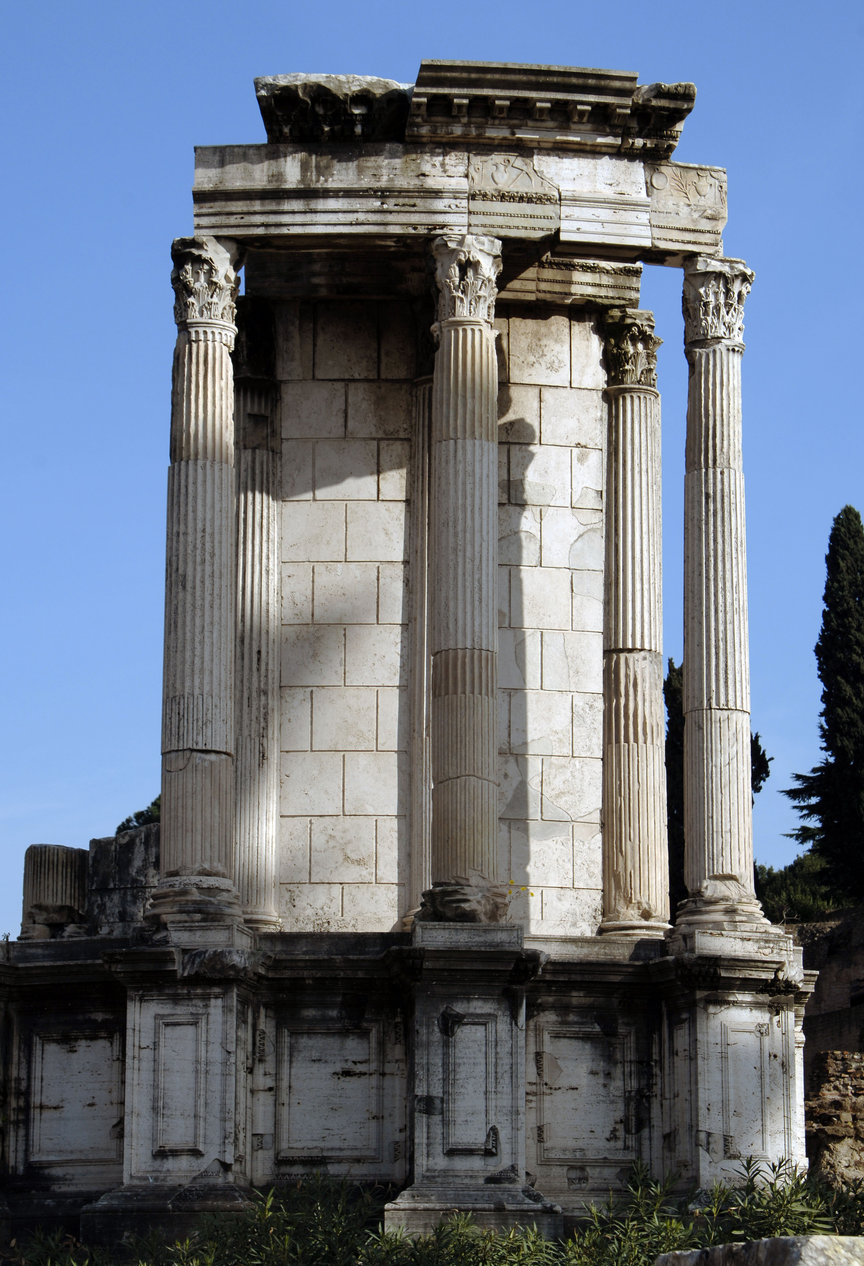 A curved stone wall fronted by four columns standing on a raised base.