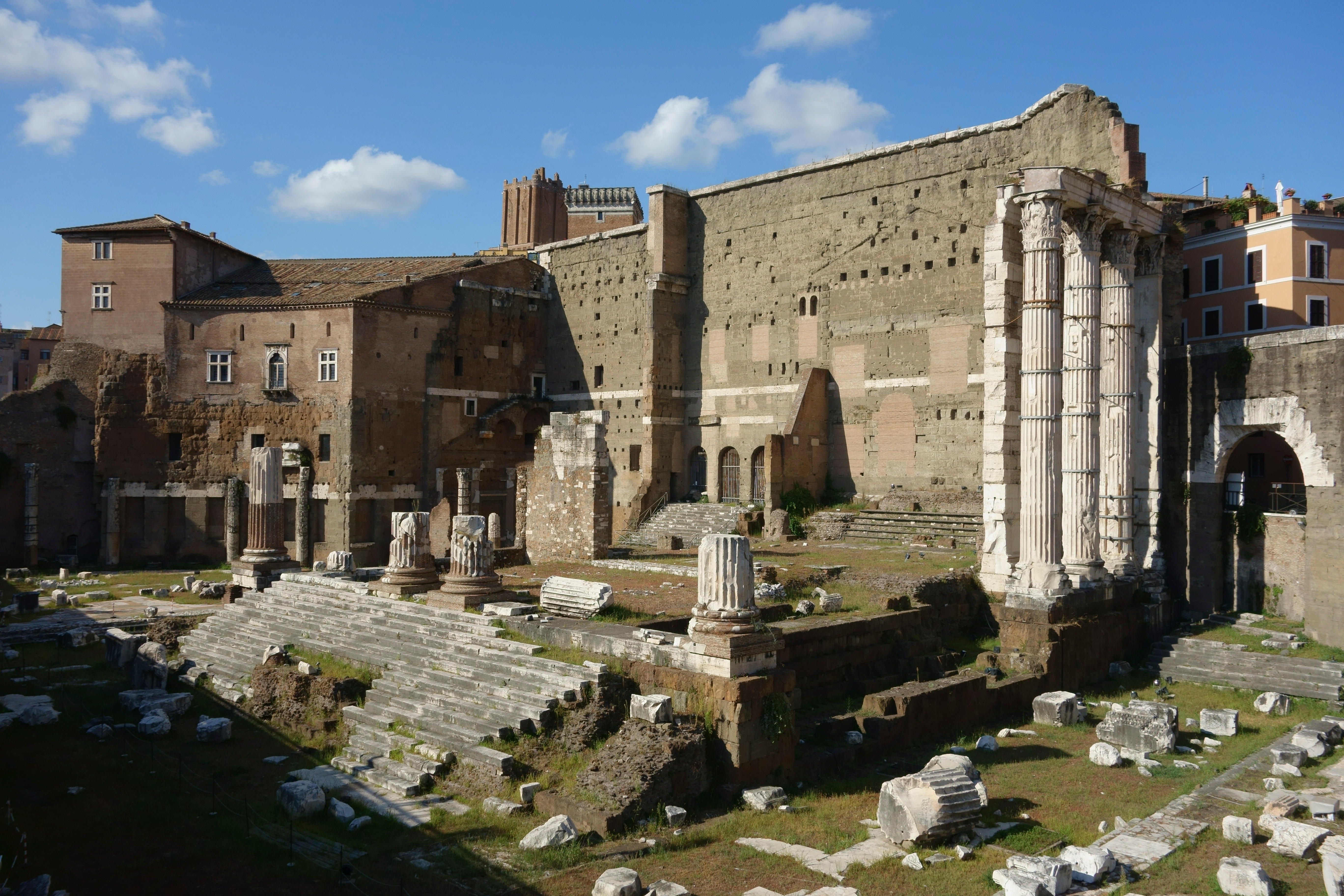 The remains of the Forum Augustus. A few columns are still standing in the foreground and a big wall towers behind.