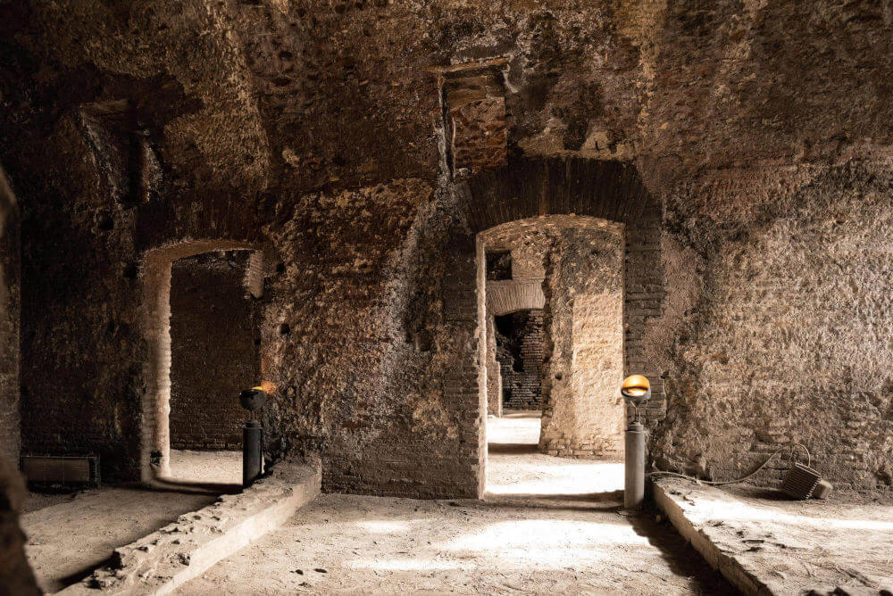 Inside a room. The walls are made of brick and it is quite dark. There are low walls where the room would have been divided into smaller spaces.