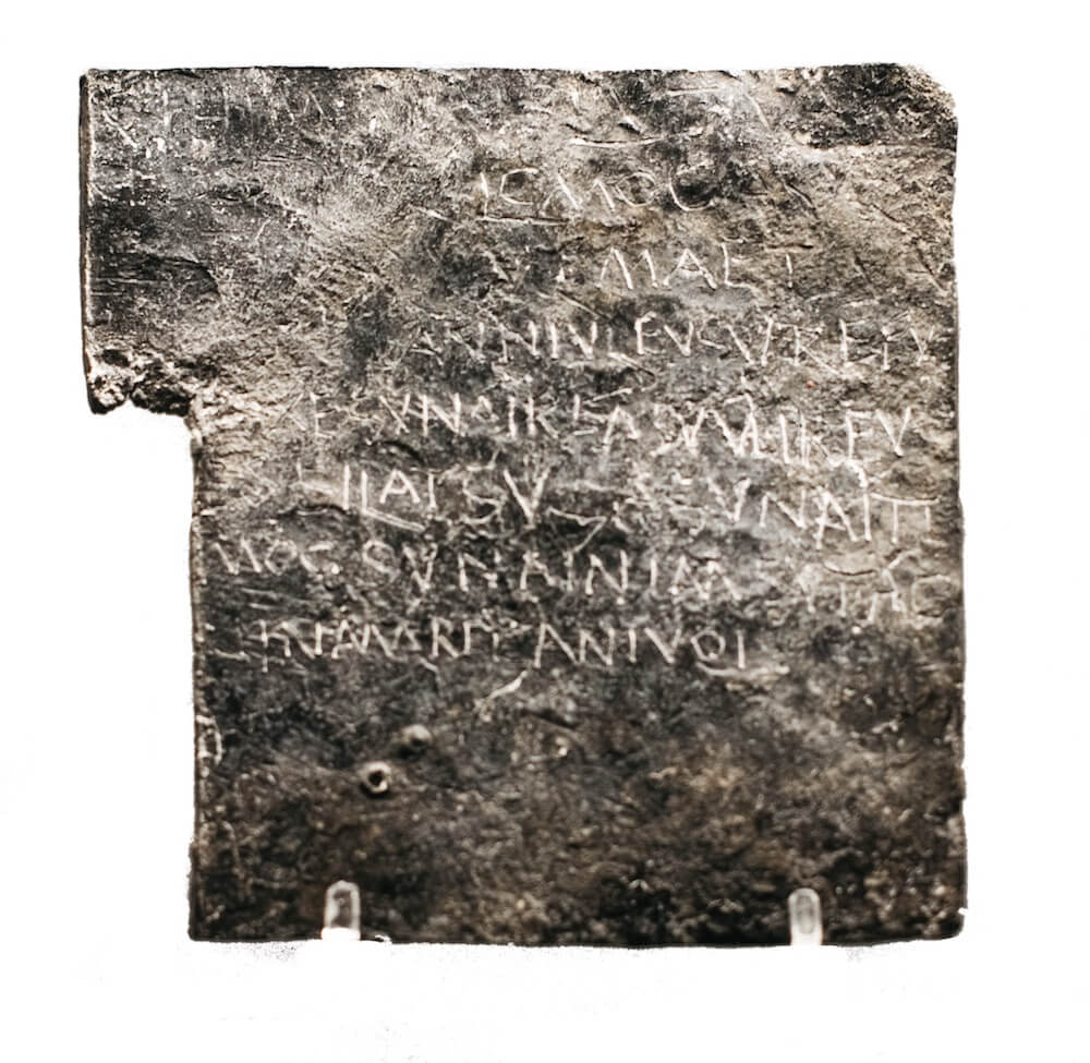 A square of metal with capital letters carved into the surface which are still just about legible.