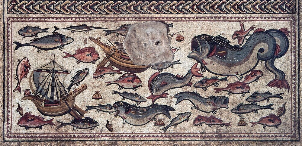 A mosaic depicting two small boats and numerous huge sea creatures, including a dolphin and a whale. One fish is about to swallow another. Scallops litter the ocean floor.