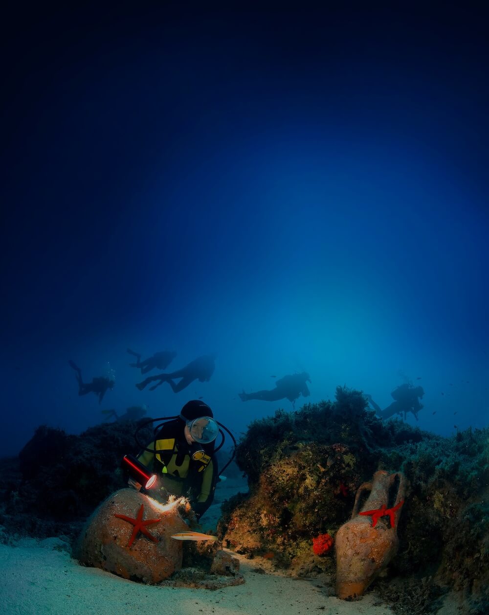 Scuba divers underwater exploring amphorae on the sea floor.