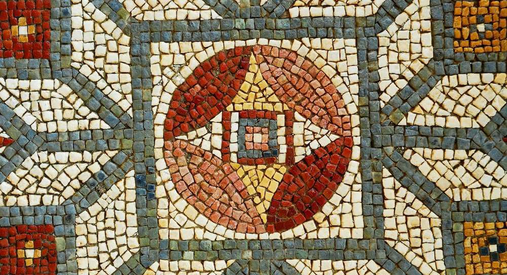 A close up of a mosaic. In the centre is a diamond surrounded by a red circle. Around that is a green square and a pattern of green and cream coming out from this.