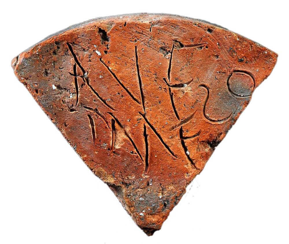 A photo of a brick. It is shaped as a quarter of a circle and has some letters carved into its surface.