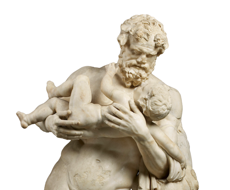 A marble statue which shows a man with a thick beard and a garland and vine leaves around his head holding a little baby and looking at it tenderly.