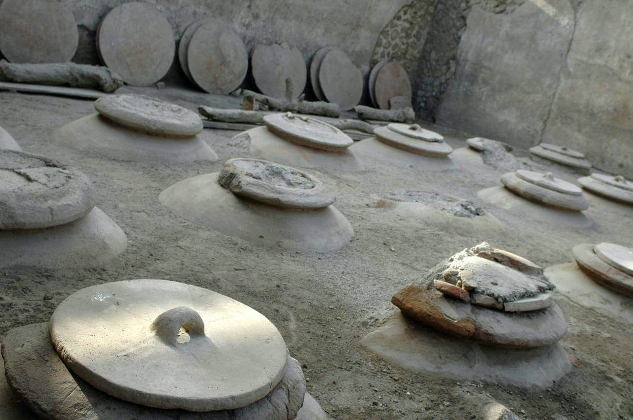 A photo showing large clay vessels half-buried in the ground. Their lids with handles sit on top.