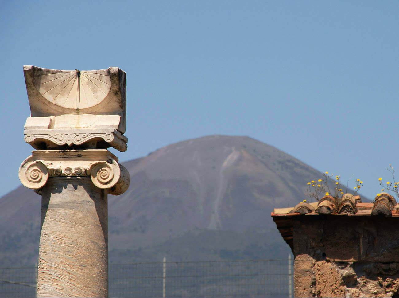 A marble column with a swirly decoration at the top. On top of the column is a block with a semi-spherical hollow. A needle sticks straight out and the sun from above casts the shadow of the needle.