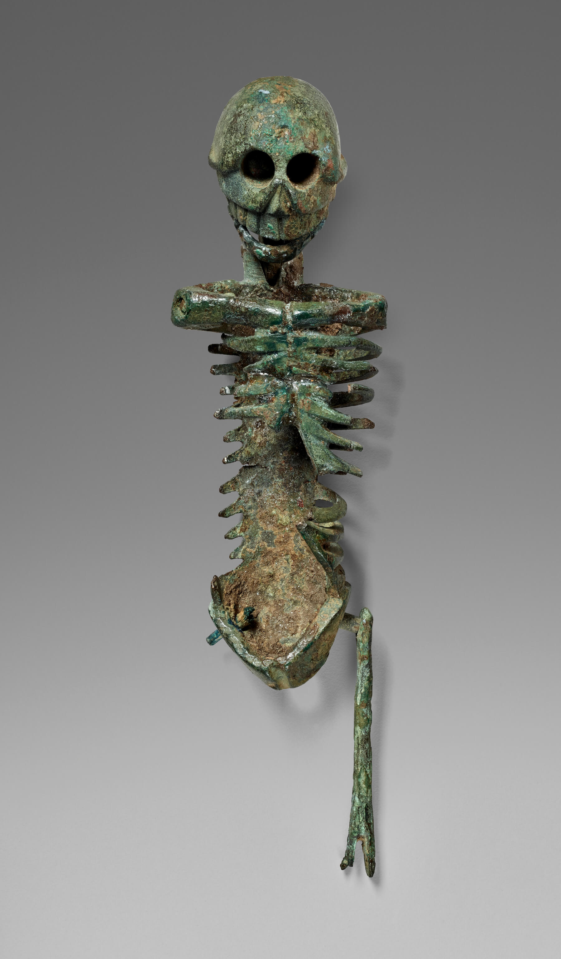 A small metal model of a skeleton. Its arms are missing and it only has one leg till the knee bone.