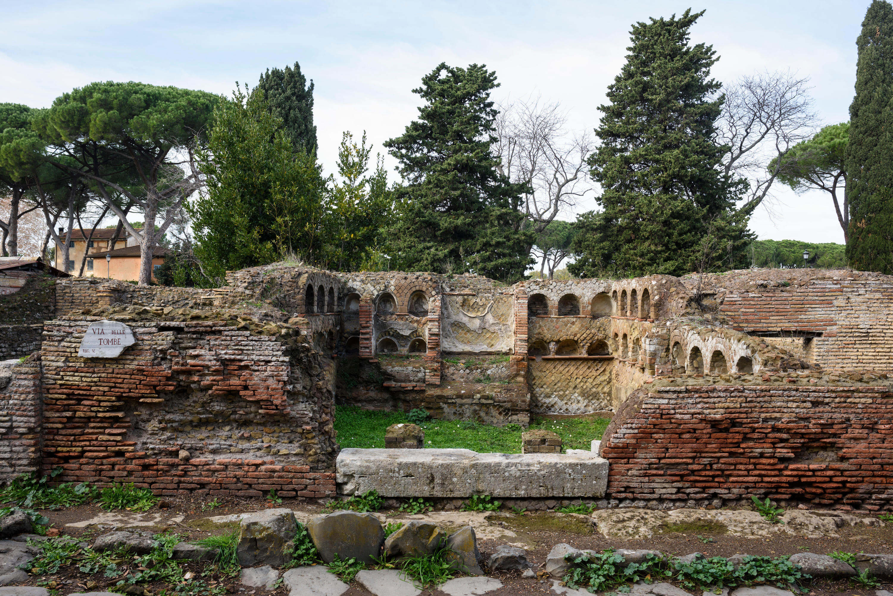 The remains of a building. It now has no roof and the walls are only about half the original height. The walls are made of brick and there are arched niches lining the inside walls.