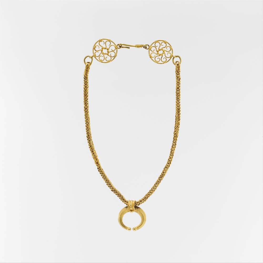 A gold necklace linked with a deocrative clasp at the top. It has a hangind pendant in the shape of a crescent moon.