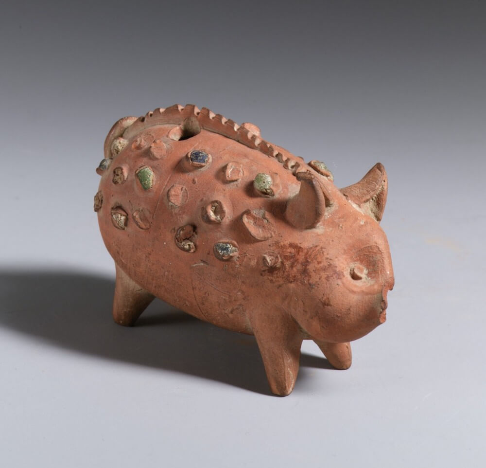 A small terracotta figurine in the shape of an animal It has short legs and pointy ears and bristles down its back.