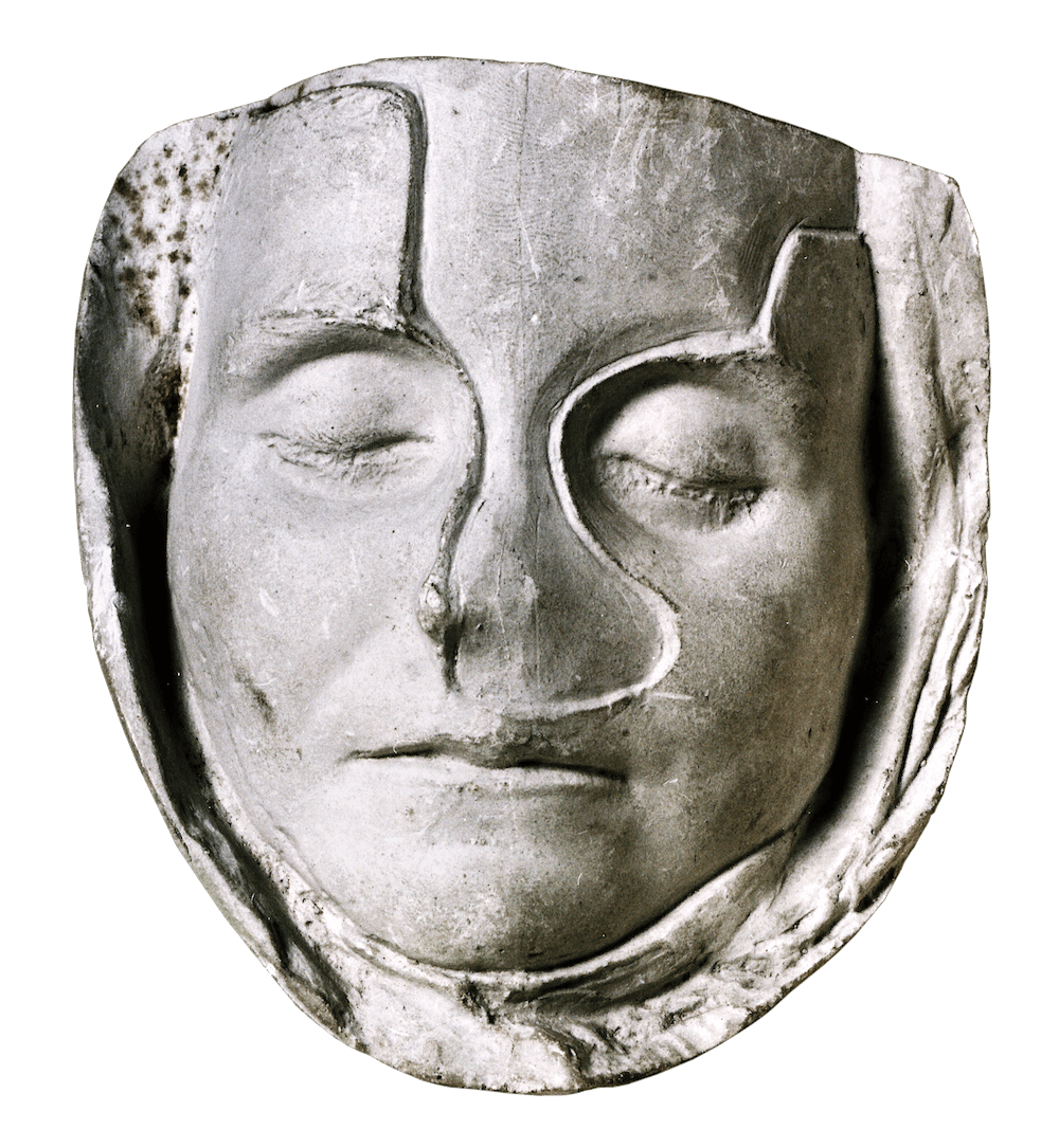The face of a young girl imprinted in plaster. Her eyes are closed.