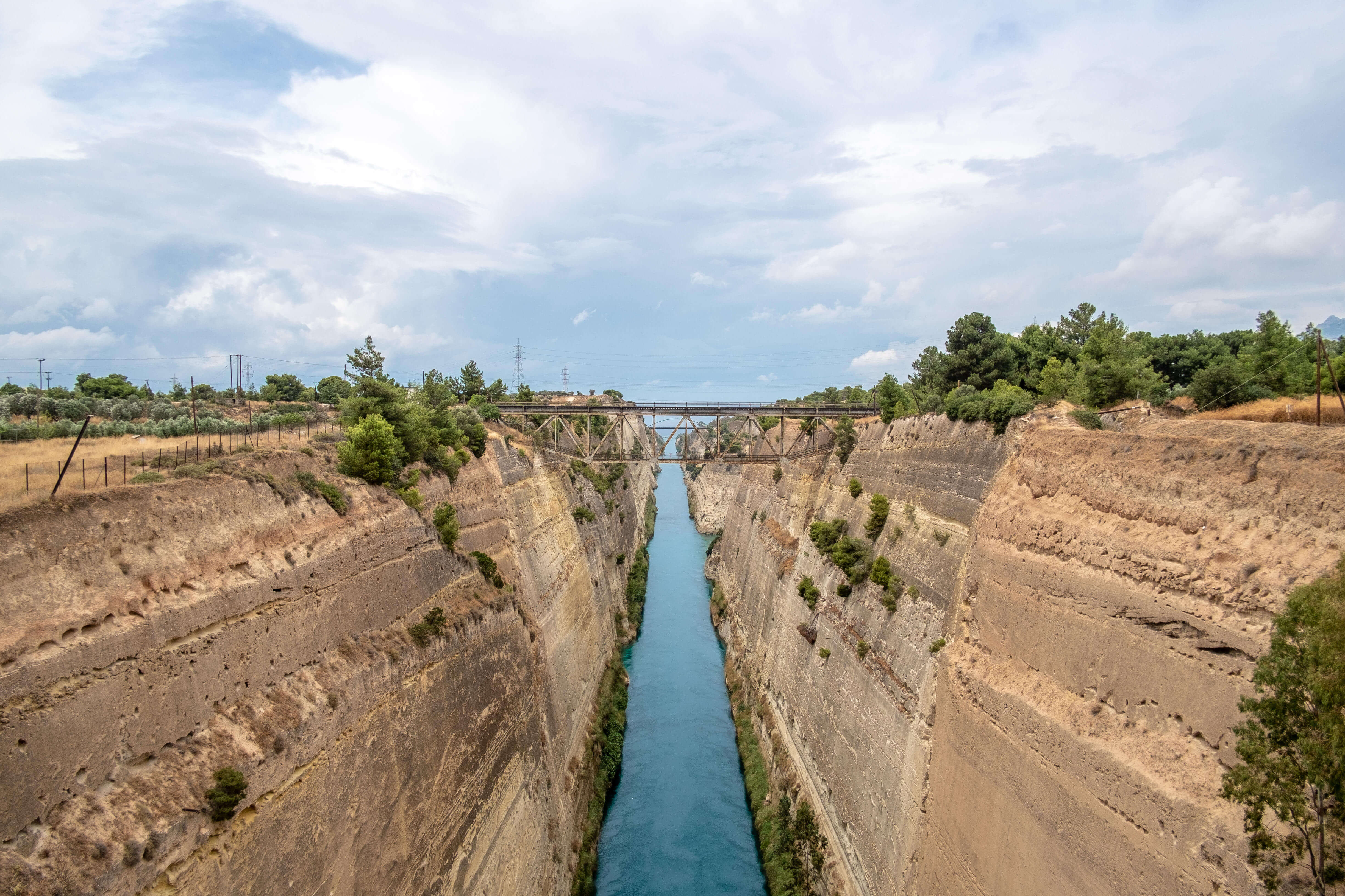 A photo of a long chasm through the land with steep sides cut in the rock. Below a canal runs towards the sea.