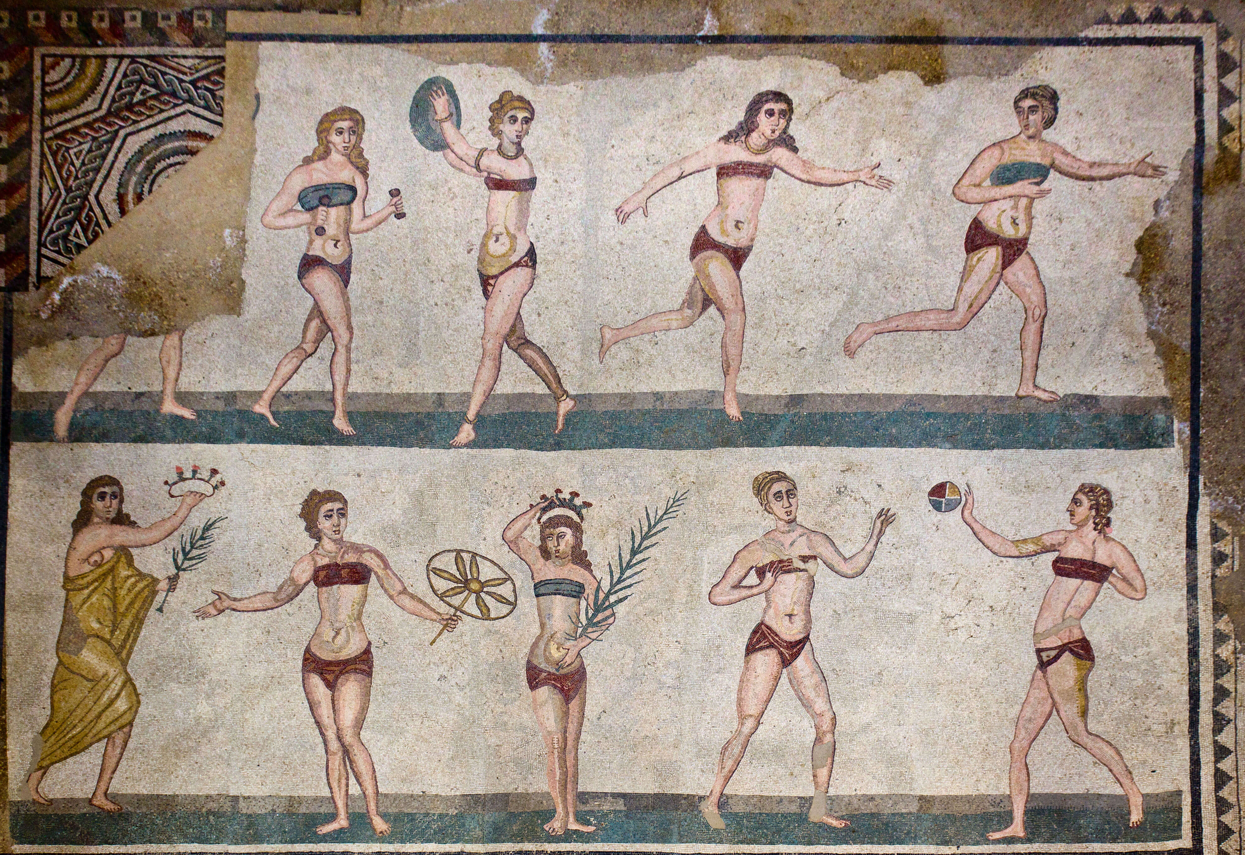 A mosaic showing women wearing bikinis. Some are holding weights or playing ball games. On the left a woman holds a palm branch.