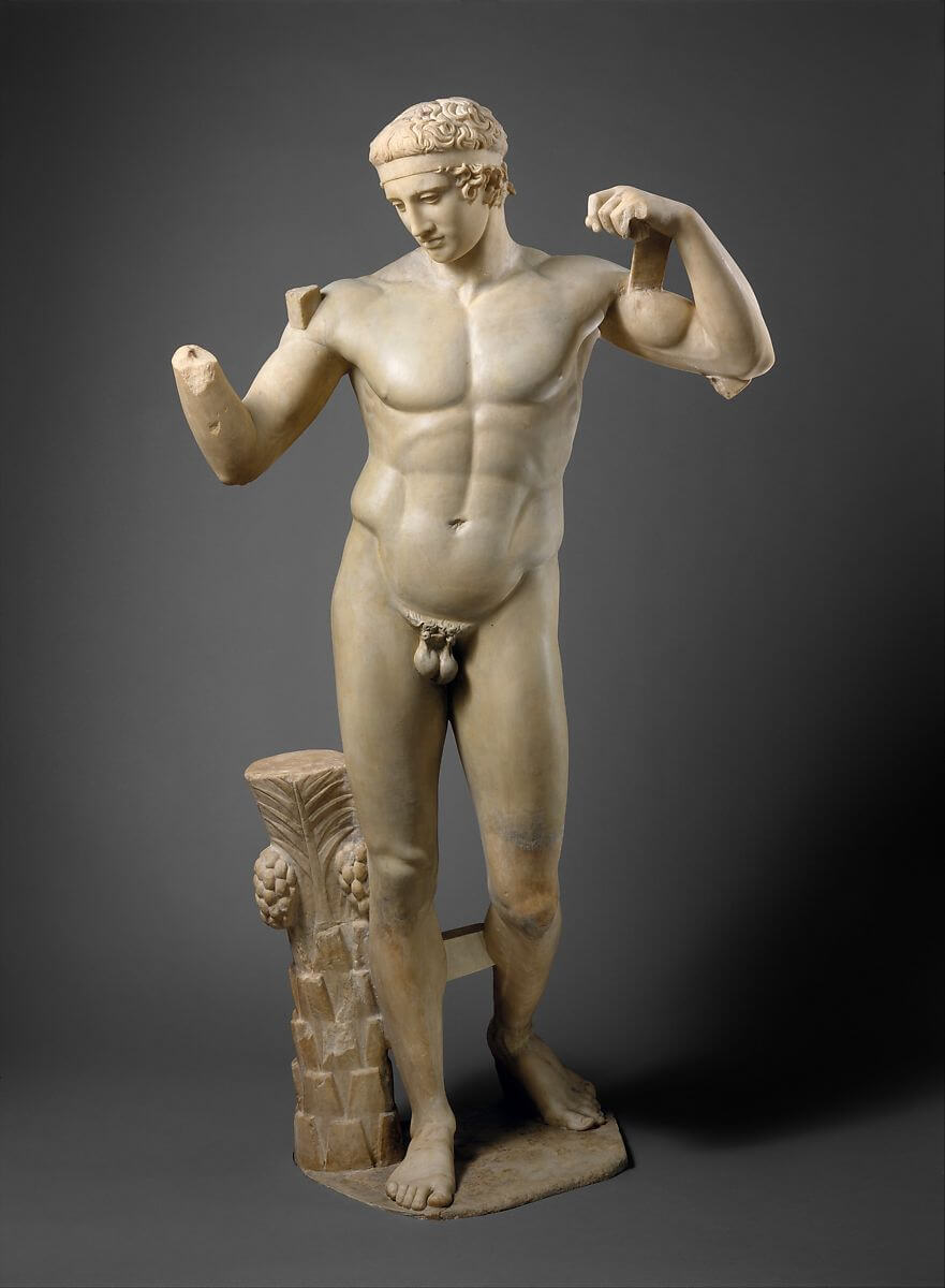 A statue of a nude young man. His arms are loosely raised to his head and his right hand is missing. A band of fabric is tied around his forehead.