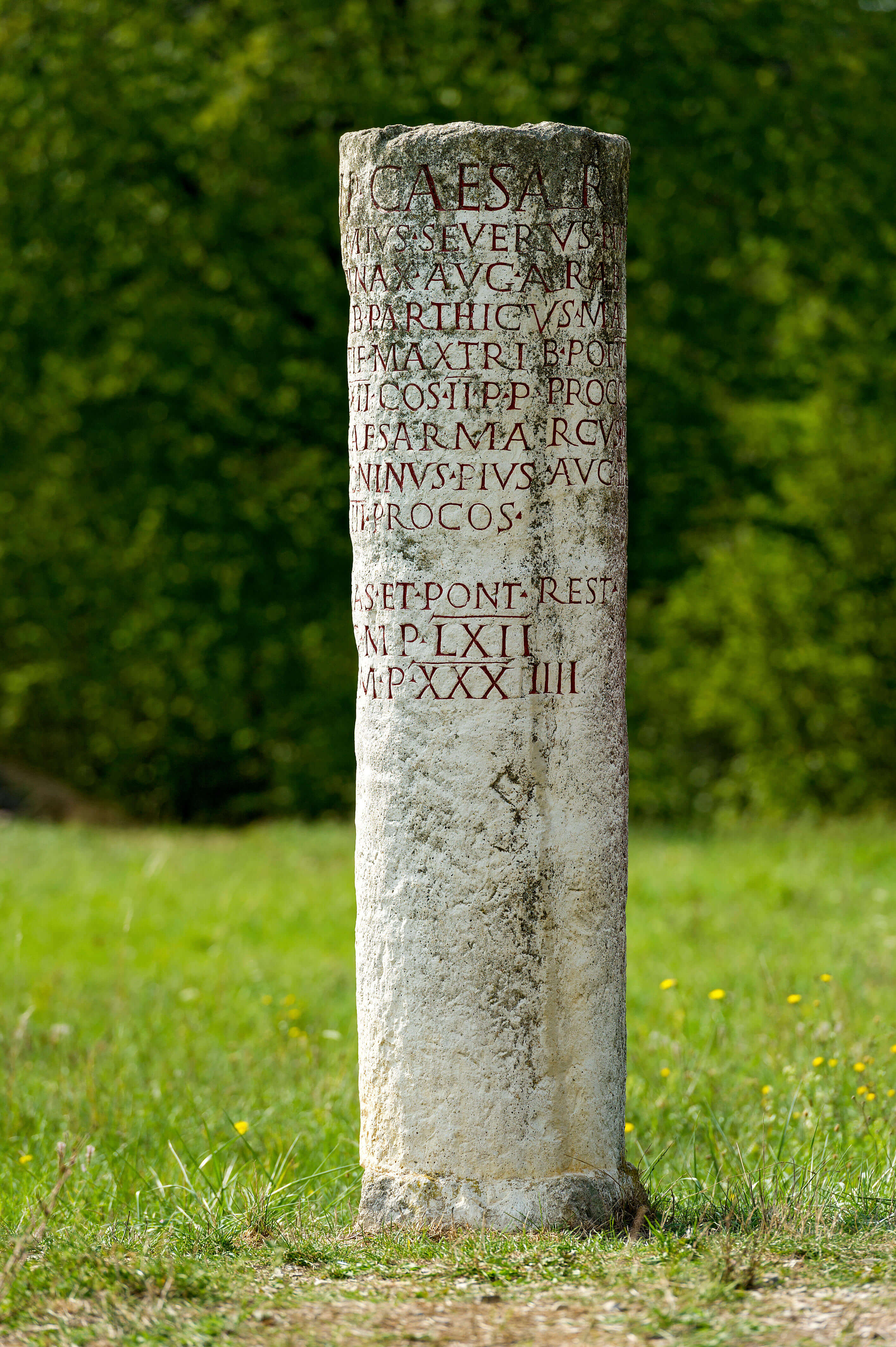 A stone cylindrical pillar with writing inscribed on it in capital letters in red.