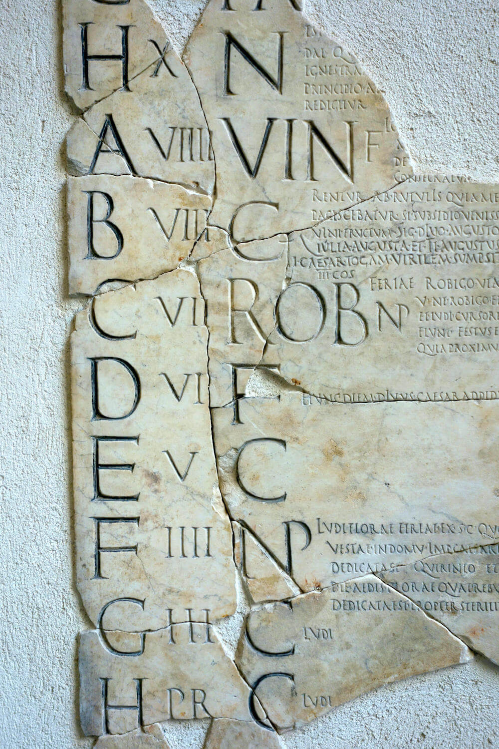 A slab of marble which is cracked into pieces. On it is carved letters, Roman numerals, and Latin text.