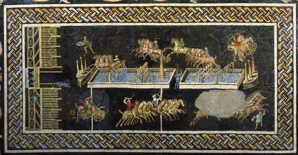 A mosaic with an intricate border showing four-horse chariots going around a race track. In the centre is a barrier filled with water. At either end are the metae.