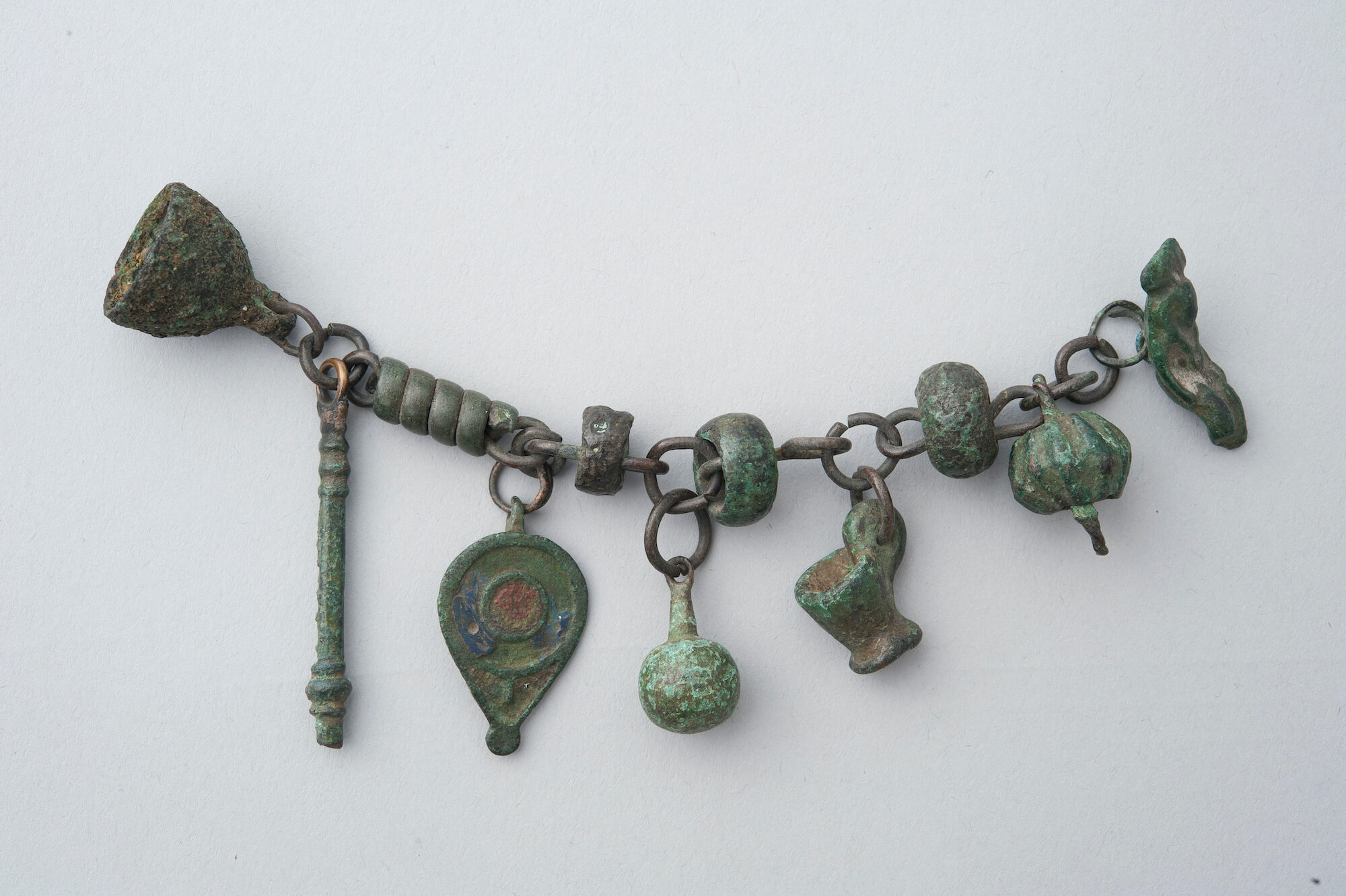 A short metal chain which has coloured a bit green wiht time. From it hang various small charms which have been worn aaway and smoothed a lot.