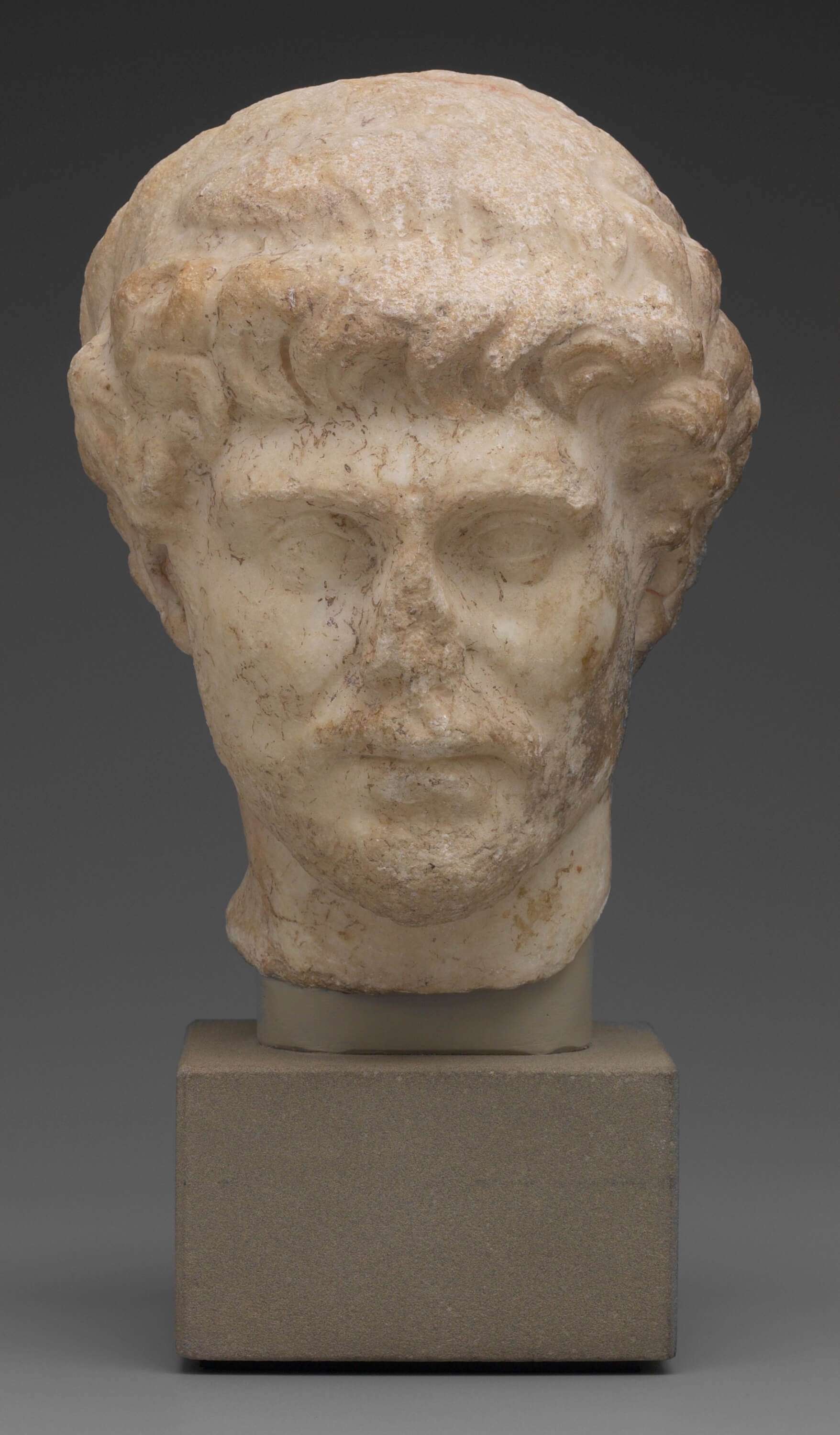 A carved stone head. It is very weathered and worn down and the features are not easily recognisable. One feature that remains is a ring of curled hair along the forehead.