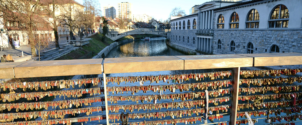 A modern bridge overlooking a river. Attached to the metal bars on the bridge are hundreds of padlocks.