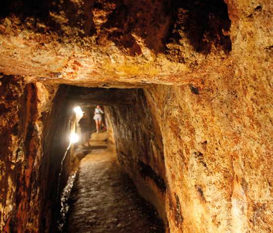 The inside of passage through an underground tunnel with rough stone walls.