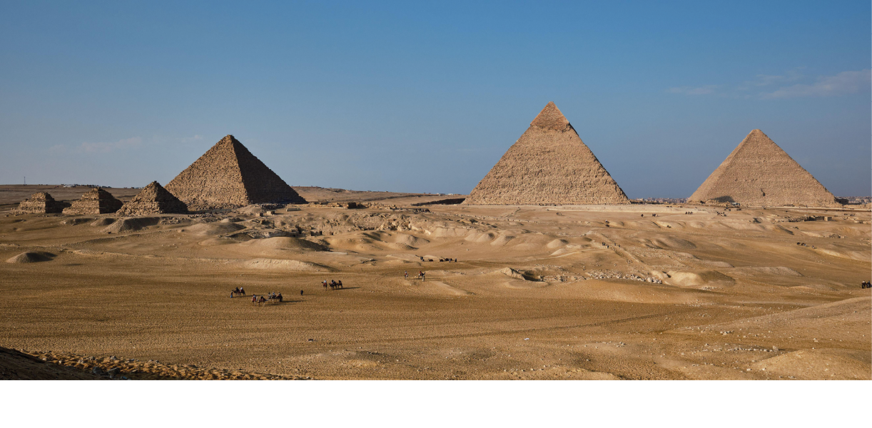 A photo of three large pyramids standing in a flat sandy desert against a blue sky.