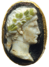 An oval disc with a dark background and gold rim. Carved into a white upper layer on the disc is a side portrait of a young man with a green garland around his head.