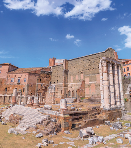A photo of the remains of a Roman temple with three columns still standing. The steps up to the temple still remain and behind it is a very tall brick wall.
