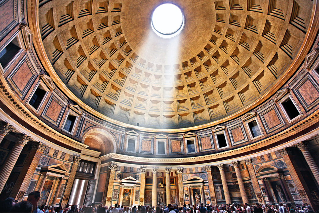 A photo from inside a round building looking up at the ceiling. It is decorated with panels and a circular hole at the center lets in a beam of light.