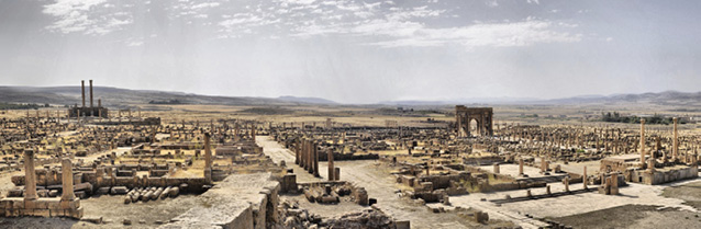 A photo showing the remains of an ancient town in a flat, desert landscape. A few pillars and arches still stand.