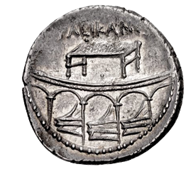 A coin showing a flat platform with four pillars. Protuding between the pillars are triangular prows. Above is a small table or stand and some letters.
