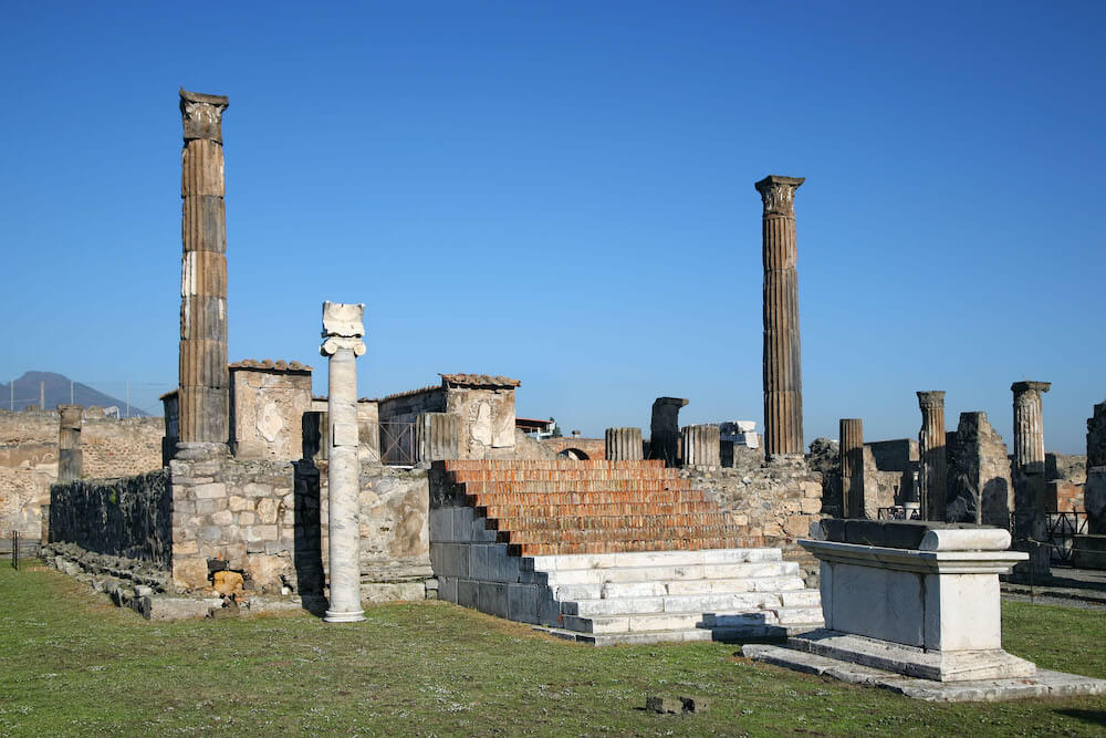 The remains of a temple. There are two columns standing on either side of a set of steps leading down to a stone altar.