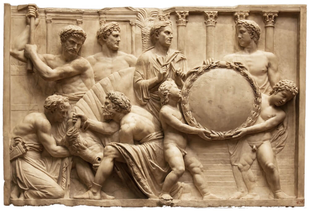 A stone carving showing two men kneeling and holding a bull by its horns, while above a man stands read to perform the sacrifice with an axe.