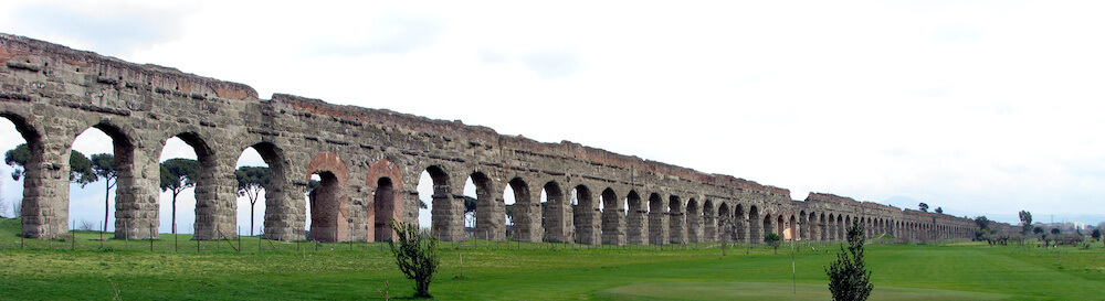 A photograph of the impressive remains of an aqueduct, with arches still standing to roughly the height of a house.