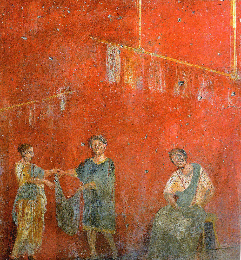 A fresco depicting three people working at a Roman laundry. One on the right is sitting down and washing clothes, another two on the right are hanging clothes up. The image has a bright red background.