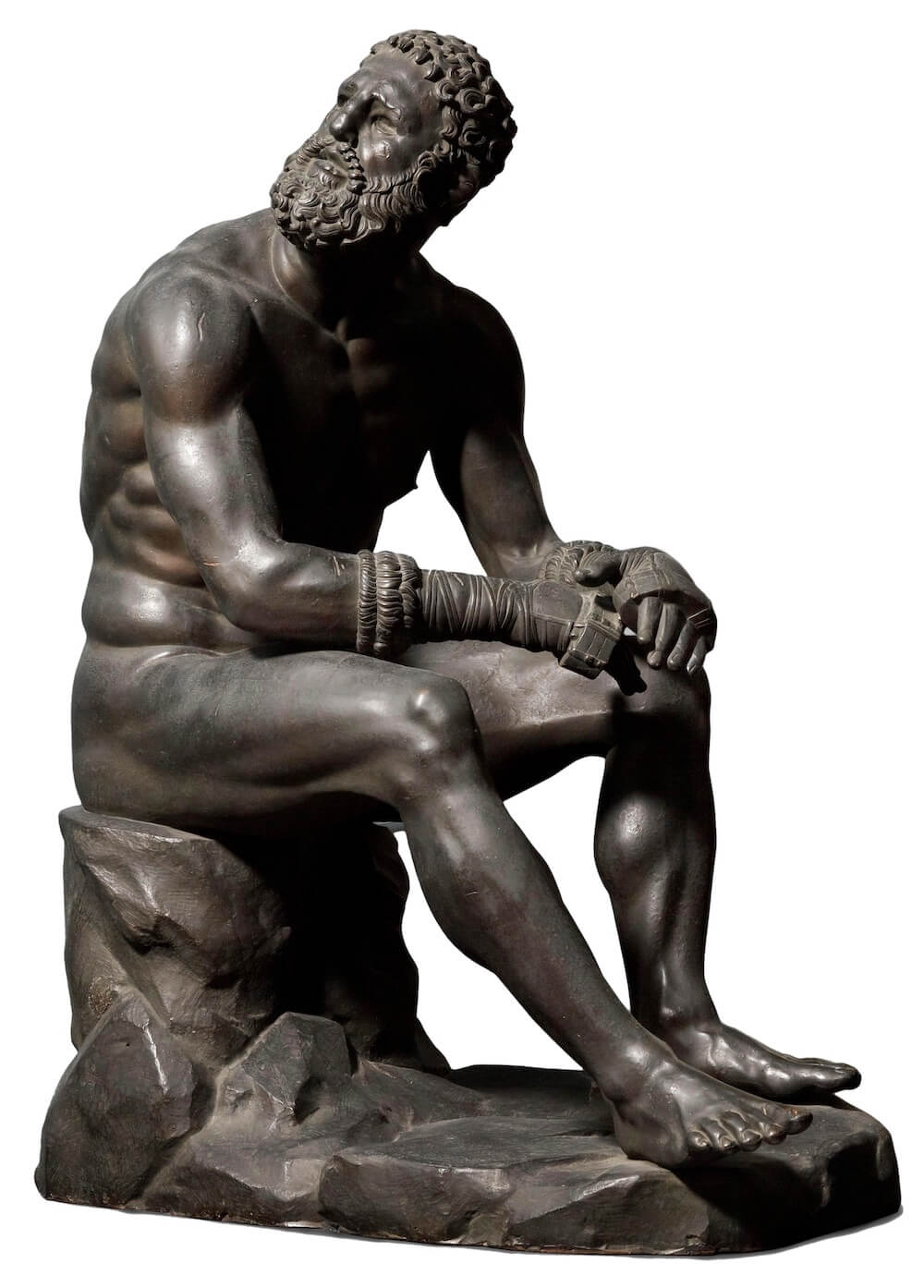 A photograph of a bronze Greek statue of a seated boxer, muscular but aging, with his head turned up and to the right, and a melancholy expression.