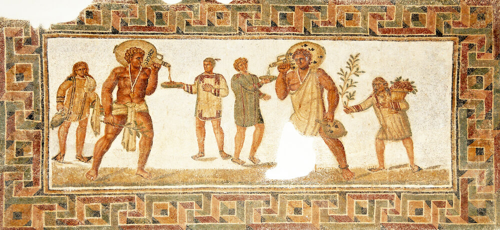 A mosaic showing two muscular slaves pouring wine into the drinking-bowls of two men, with a couple more standing round about.