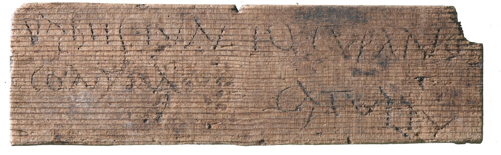 A wooden tablet with some writing roughly scratched into it.