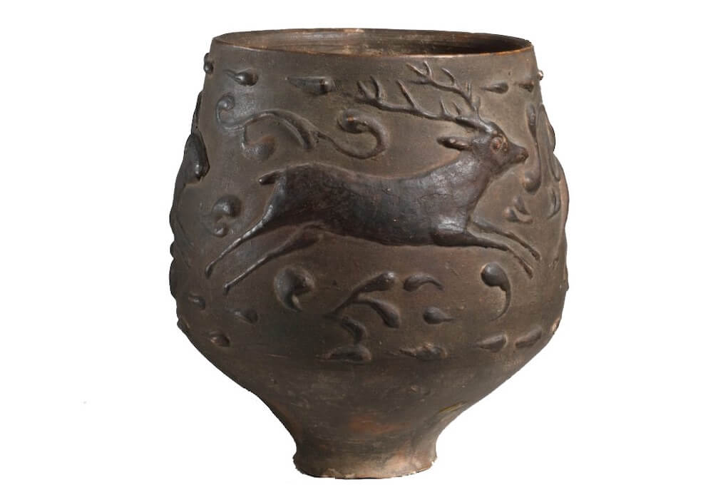 A small terracotta cup with a stag depicted on the front.