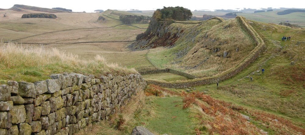 A photograph of Hadrians Wall stretching out across the brown moors of Northumberland, winding up and down rocks and fells, on a misty day.