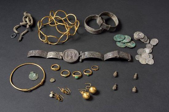 A selection of gold and other metal jewellery and coins laid out on a dark surface.